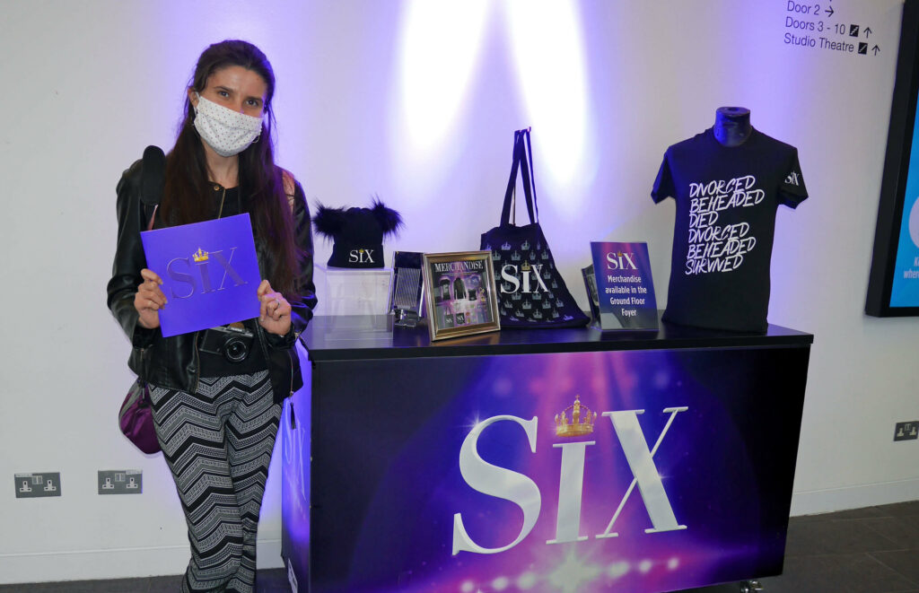 Kat Masterson standing next to merchandise for SIX the Musical at The Marlowe Theatre in Canterbury, Kent