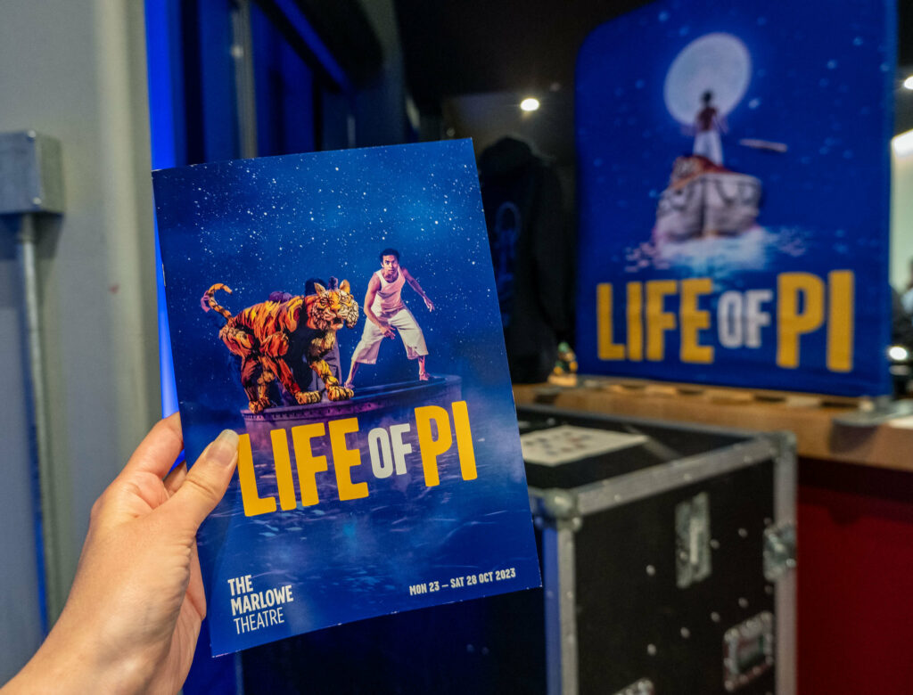 Life of Pi programme in front of a promotional poster at The Marlowe Theatre in Canterbury, Kent