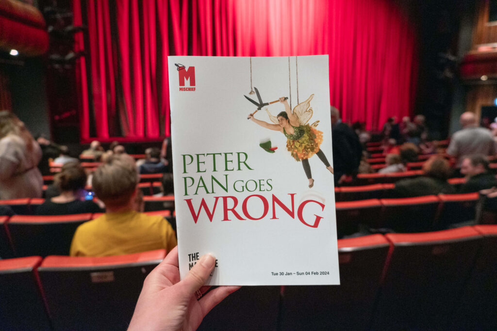 Peter Pan Goes Wrong programme in front of The Marlowe Theatre stage, Canterbury