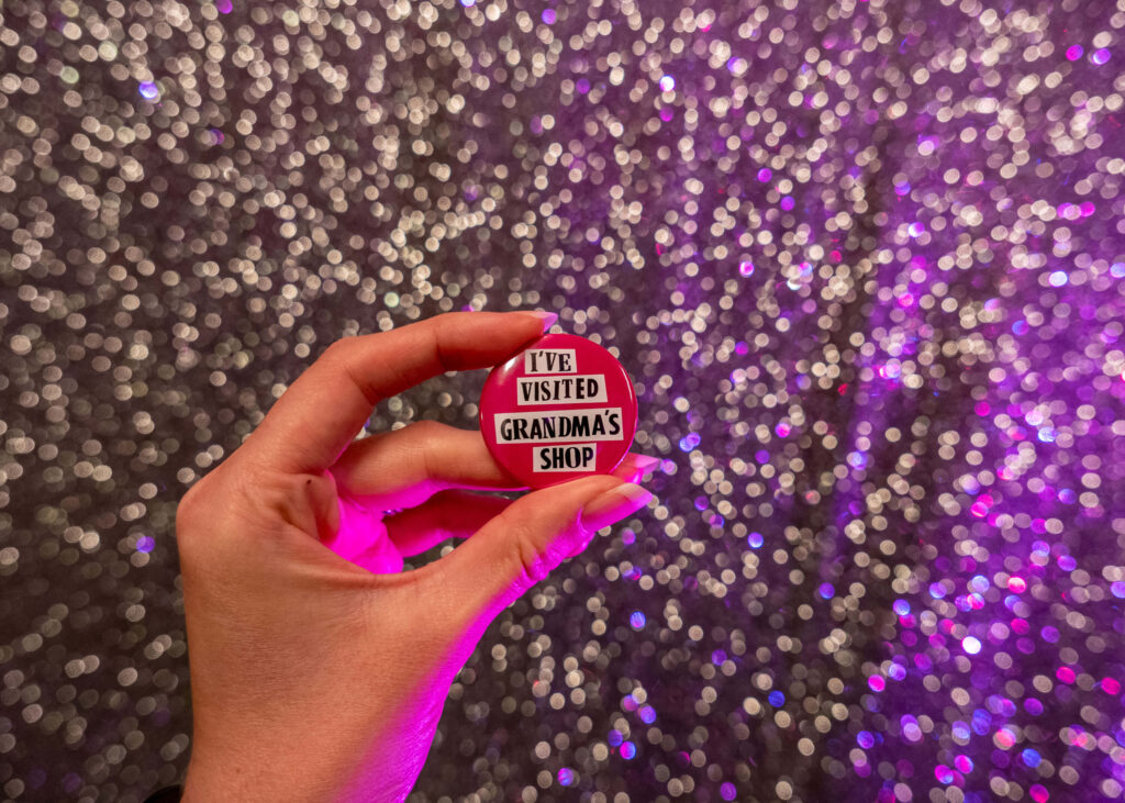 Julie Flower: Grandma's Shop badge in front of the Gilded Balloon Patter House glitter wall | Edinburgh Fringe