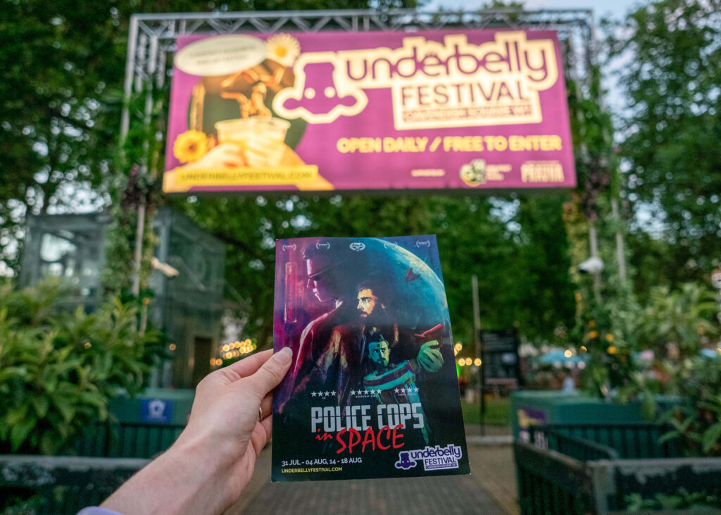 Police Cops in Space leaflet in front of the Underbelly Festival sign, Cavendish Square